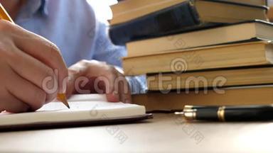 学生正在用一张桌子上放着一堆书的钢笔写作。