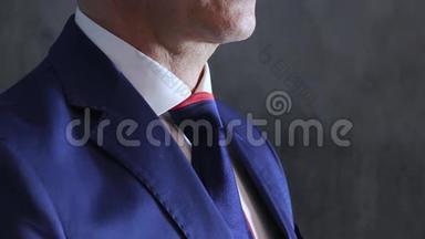 男人`手臂调整蓝色领带在喉咙靠灰色的墙壁，侧视