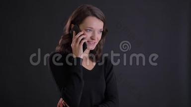 年轻迷人的白种人长发女孩在黑色背景的智能手机上微笑交谈的照片。