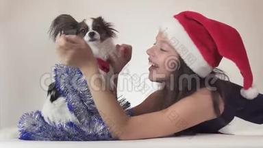 圣诞老人戴着圣诞老人的帽子、戴着狗的美丽的少女在新年里`他的小罐子快乐地玩耍