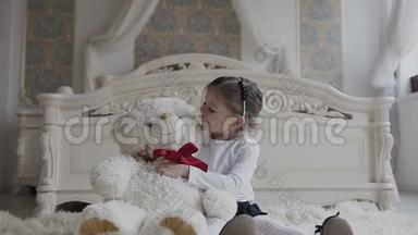 漂亮的小女孩坐在卧室的软地毯上，带着一只大玩具软熊