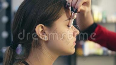 化妆师在一个年轻女孩的脸上涂上遮瑕膏。 完美妆容的基础。 慢镜头