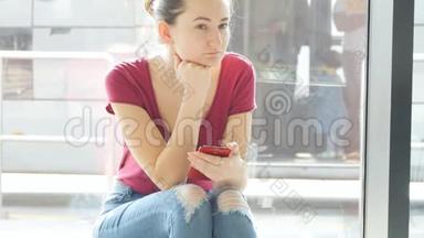 年轻女子坐在机场候机室的窗户附近，<strong>环顾四周</strong>，然后使用智能手机。 预期