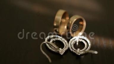 近景黄金结婚戒指和银色新娘耳环与钻石在桌子上。