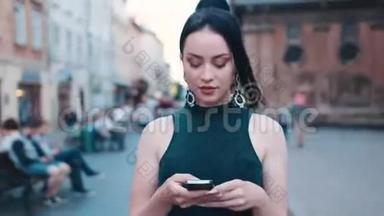 自信、漂亮、蓝眼睛、深褐色头发的女人穿着时尚的服装走在市中心的一条街上，用她€™手机