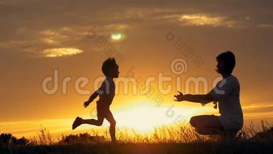 一个快乐的小男孩的剪影跑进他慈爱的母亲的<strong>怀里</strong>，在夕阳面前拥抱。