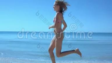 美丽苗条的比基尼女郎沿着海边的海滩奔跑，头发随风飘扬，奔跑