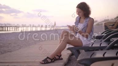 一位卷发<strong>女士</strong>在手机上打印了一条信息，一位<strong>女士</strong>坐在靠近大海的休息室里，身后是一个荒芜的人