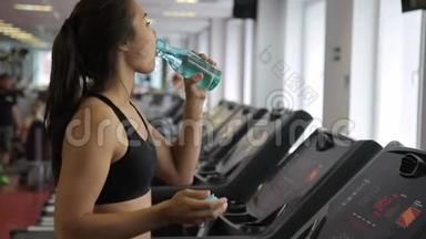 女运动员在跑步机上行走，在室内运动俱乐部喝水。