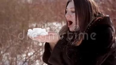 戴着眼镜和貂皮大衣的快乐女孩把手里的雪吹得通红
