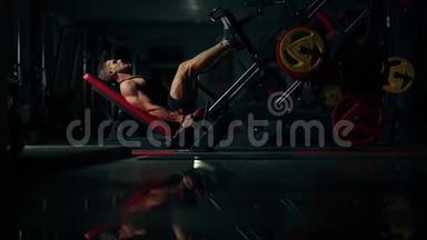 一个<strong>肌肉</strong>发达的人在黑暗的健身房里用运动训练器械锻炼<strong>腿部肌肉</strong>，举重