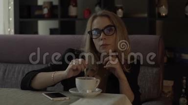 一位戴眼镜的年轻女商人在咖啡杯里<strong>用勺子</strong>搅拌糖