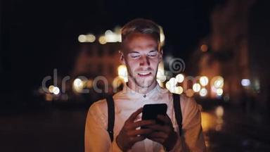 年轻迷人的男人用智能手机走在夜城的街道上。 交流、旅游、旅游、约会、商务