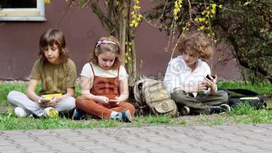两个兄弟和一个妹妹坐在草地上使用智能手机。 在社交网络中社交。 网络依赖