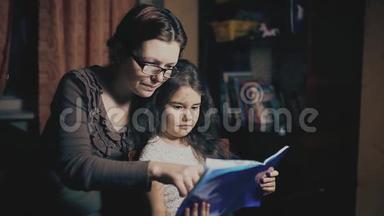 小女孩和一个成年女人正在读一本书，他们在晚上被教一个睡前故事。 母亲和