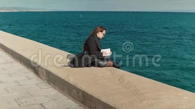 女人在海边的户外素描书上画素描。 慢镜头