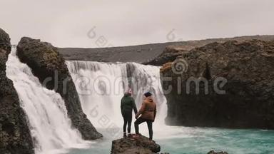 自由：徒步旅行后，幸福的一对夫妇站在冰岛瀑布附近，<strong>一起举手</strong>。