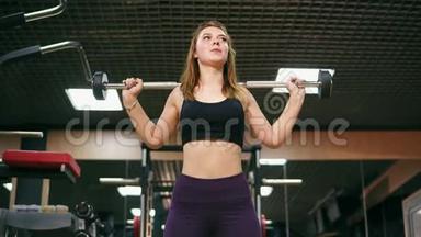 一位<strong>身材矮小</strong>的年轻女子在健身房里用杠铃做蹲，改善了她的肌肉