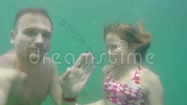 白种人的男人和女孩潜入海里，在水下的镜头中挥动他们的手