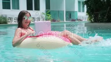 年轻女子在海里游泳，在游泳圈里游泳。 女孩躺在游泳池里，用电脑在一个充气的圆圈上，顶部