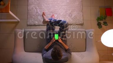 在舒适的家中，年轻人坐在沙发上用绿色屏幕的手机进行特写镜头