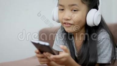 亚洲小女孩用白色无线耳机听音乐，用幸福说话，竖起大拇指，看着相机