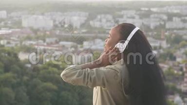 迷人的非裔美国女孩听音乐，感到快乐。 微笑着年轻的黑人女孩模糊的城市背景