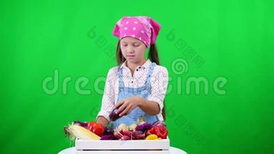 可爱，微笑，小农家姑娘出示一盒不同新鲜蔬菜，收获.. 在工作室的绿色背景上
