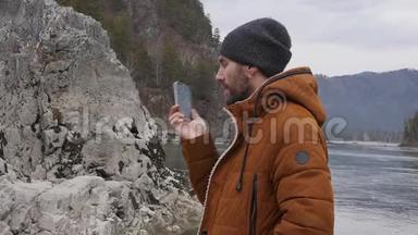大胡子的游客正在与朋友在一条山河畔的手机上举行视频会议。 慢动作