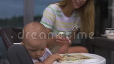 年轻的母亲喂养她的小儿子坐在孩子的座位上-家庭价值观温暖的颜色夏天的场景