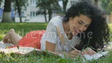 漂亮的卷发黑发女郎在公园里的格子上放松，写了一封信
