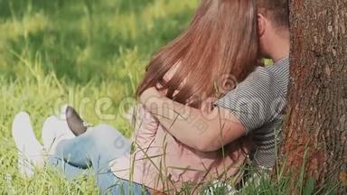 一对相爱的情侣，拥抱在一起，坐在公园的树下。后视图。