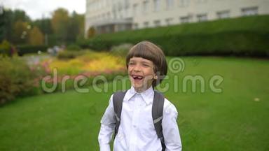 一年级学生玩得开心，带着背包在户外对着镜头笑的可爱男孩的画像