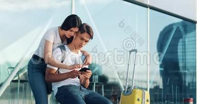 使用智能手机相爱的幸福夫妇。 年轻的已婚夫妇<strong>在机场</strong>等待航班时玩得很开心。 那个女人