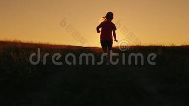 无忧无虑的女孩在日落的背景下跑上山。 克服困难，首先取得成就