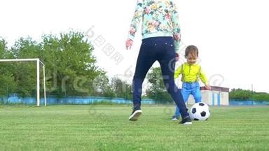 快乐的母亲和孩子在绿色草坪上缓慢地用足球踢足球。 幸福家庭的概念