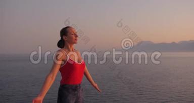 穿红色衣服的白人妇女在日落时在海边的悬崖上练习瑜伽，放松身心。