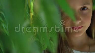 漂亮的年轻女孩看着绿树旁的照相机。 慢慢地