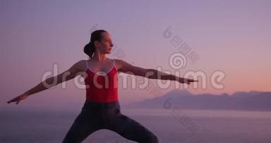 穿<strong>红色</strong>衣服的白人妇女在日落时在<strong>海边</strong>的悬崖上练习瑜伽，放松身心。