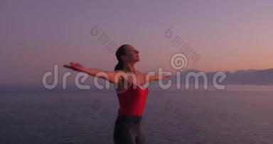 穿红色衣服的白人妇女在日落时在海边的悬崖上练习瑜伽，放松身心。