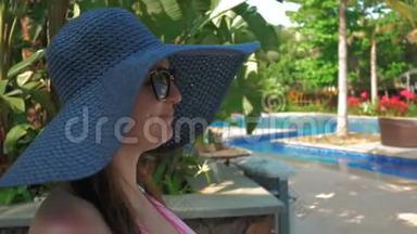 戴着蓝色帽子的漂亮女孩走到游泳池旁的休息室。 夏日的阳光。 慢动作