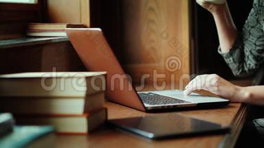 一个女人正在图书馆用笔记本电脑工作。 旁边是书，特写——只有手在画框里可以看到