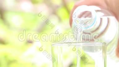 女人手拿水瓶，在模糊的绿色自然背景上向玻璃中倒入清澈的饮用水。