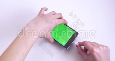 白色背景下带有绿色彩色按键屏幕的女士双手连接电缆至智能手机