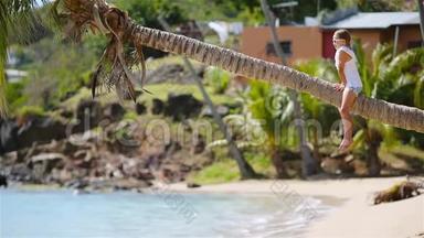 暑假期间<strong>坐在</strong>棕榈<strong>树上</strong>的热带海滩上可爱的小女孩的后景