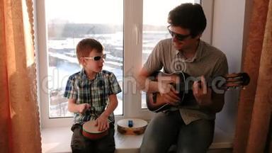 戴着太阳镜演奏<strong>乐器</strong>。 爸爸在弹吉他，儿子坐在窗台上打<strong>鼓</strong>。