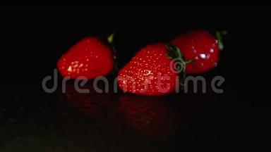 三个草莓浆果在黑暗中躺在潮湿的表面上。 黑色背景