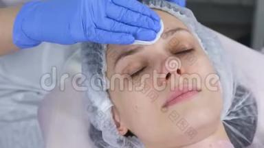 美容师用棉垫擦拭一个年轻女人的脸。 美容师戴手套和面部特写