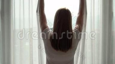 穿白色t恤的女人揭开窗帘，看着窗外。 在外面欣赏海景
