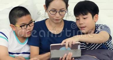 快乐的亚洲家庭姐妹和兄弟与朋友玩平板电脑在家微笑着面对。